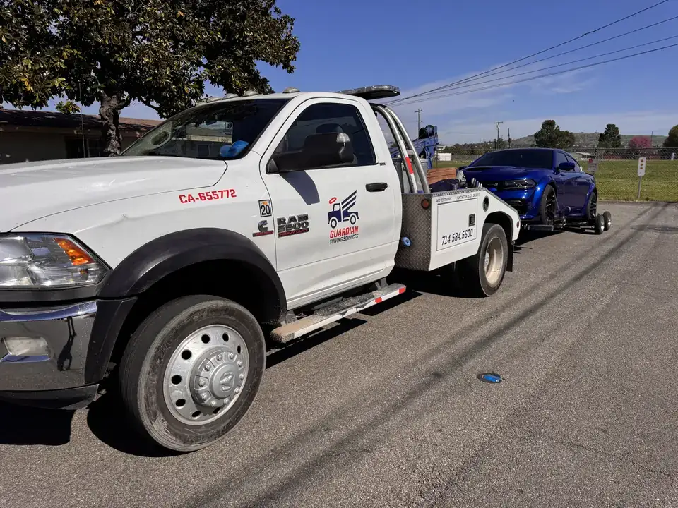 Guardian Towing Ram 5500 tow truck with a blue Dodge Charger on wheel dollies